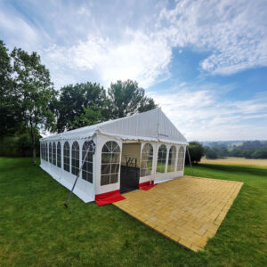 Hvidt festtelt på 6x9 meter opstillet på grøn græsplæne omgivet af bakket landskab og træer.